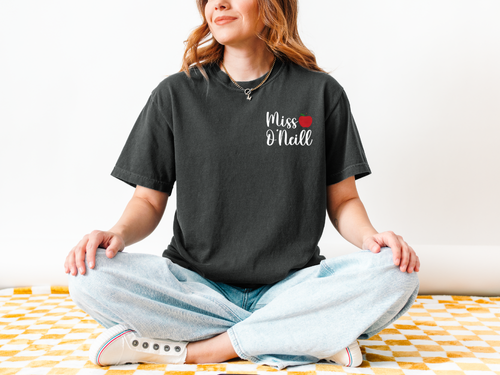 Person wearing a black t-shirt with 'Miss O'Neill' text, sitting on a yellow and white checkered blanket.